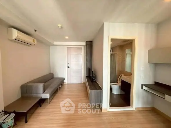Modern apartment interior with cozy living room and adjacent bathroom, featuring sleek furniture and wooden flooring.
