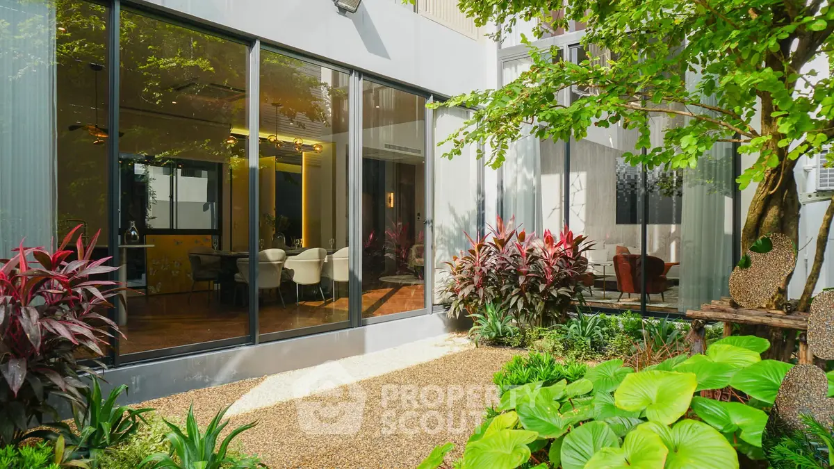 Modern home with lush garden and large glass windows showcasing interior elegance.