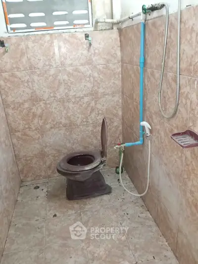 Simple bathroom with tiled walls and floor, featuring a basic toilet and shower setup.