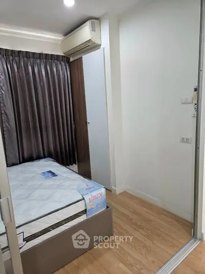 Cozy bedroom with wooden flooring and air conditioning, featuring a comfortable bed and elegant curtains.