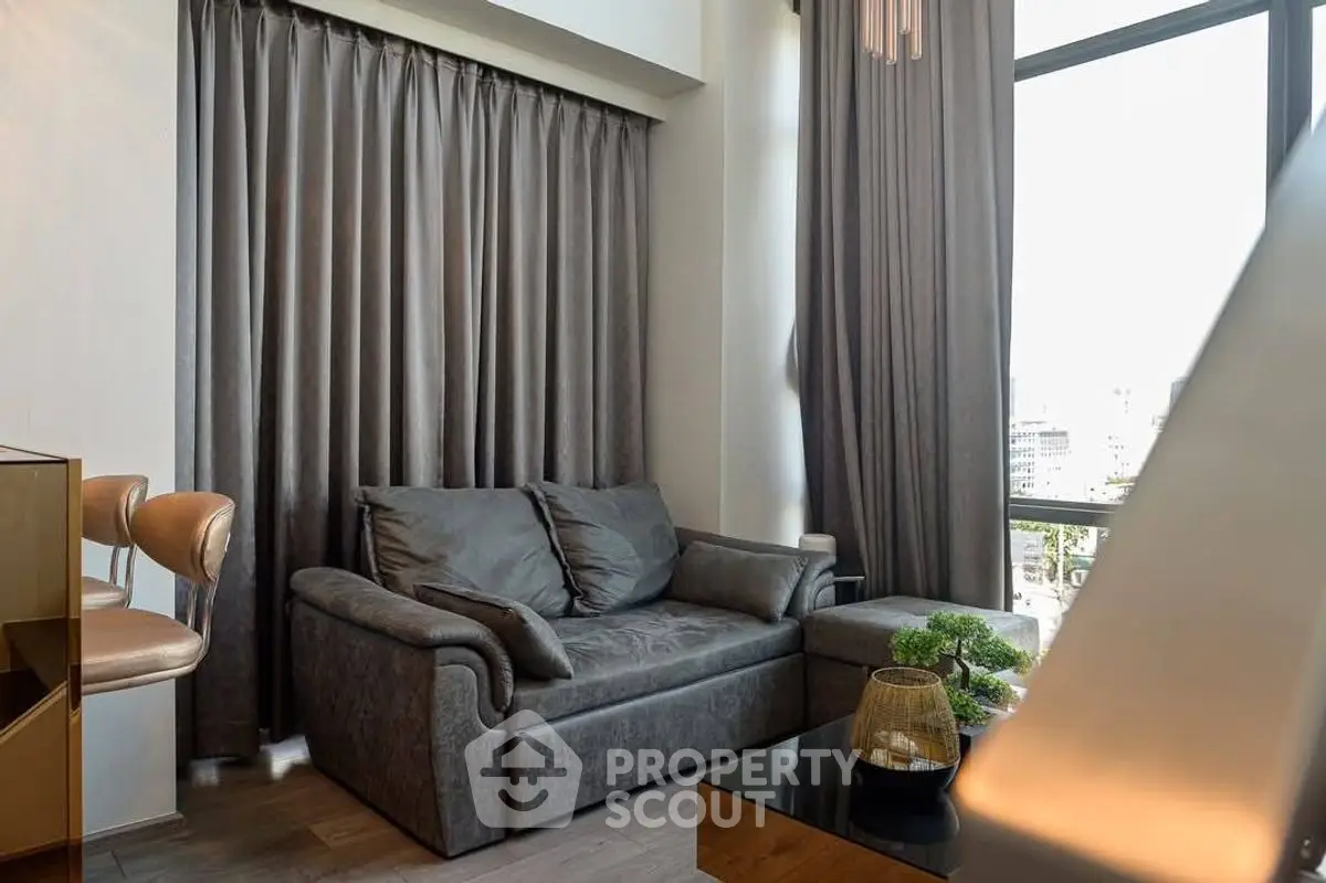 Modern living room with sleek gray sofa and floor-to-ceiling windows offering city views.