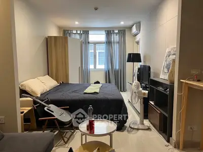 Modern studio apartment with cozy bed, stylish decor, and natural light from large window.