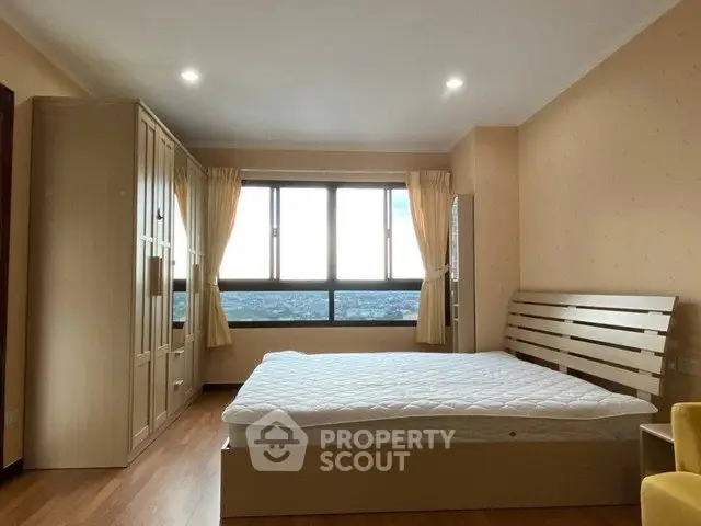 Spacious bedroom with large window offering stunning city views, featuring a comfortable bed and ample wardrobe space.