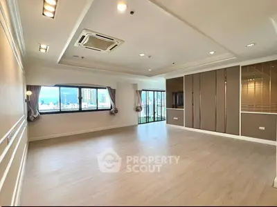 Spacious modern living room with large windows and city view, featuring elegant ceiling design and wooden flooring.