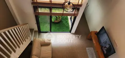 Modern living room with high ceiling and garden view, featuring a cozy sofa and wall-mounted TV.
