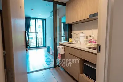 Modern apartment kitchen with sleek wooden cabinets and open layout leading to a bright living area.