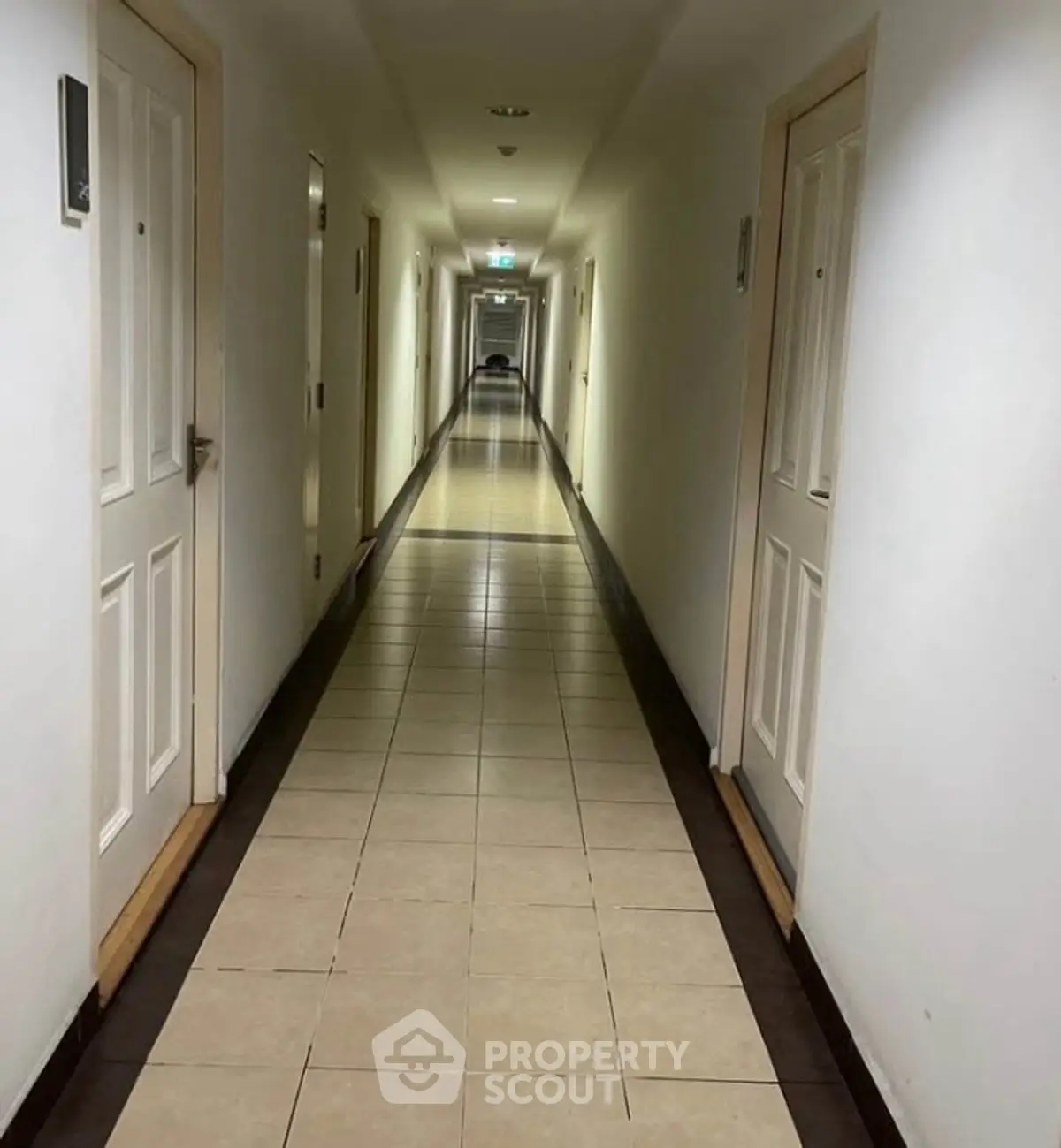 Long corridor in a residential building with tiled flooring and multiple doors.