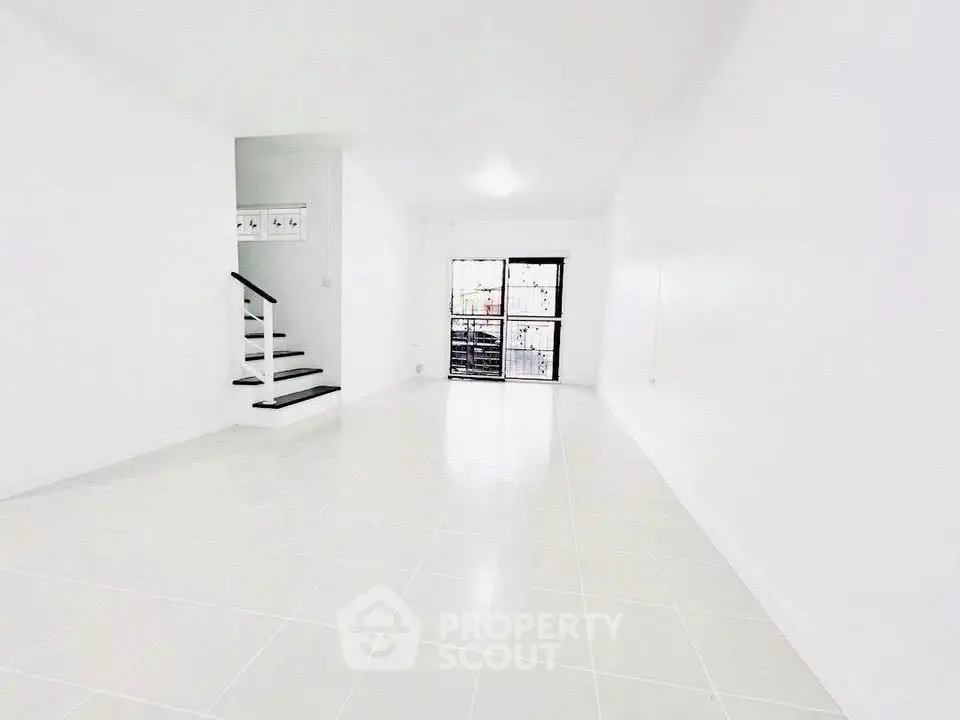 Spacious white minimalist living room with staircase and large window
