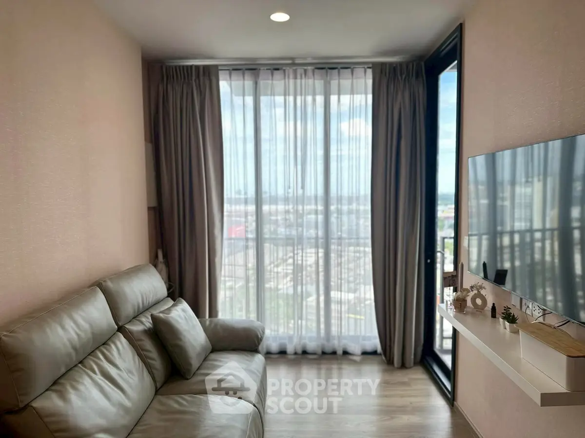 Modern living room with large window and city view, featuring a sleek sofa and wall-mounted TV.