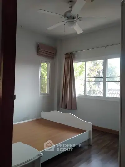 Cozy bedroom with ample natural light, featuring a single bed frame, ceiling fan, and air conditioning unit, ideal for comfortable living.