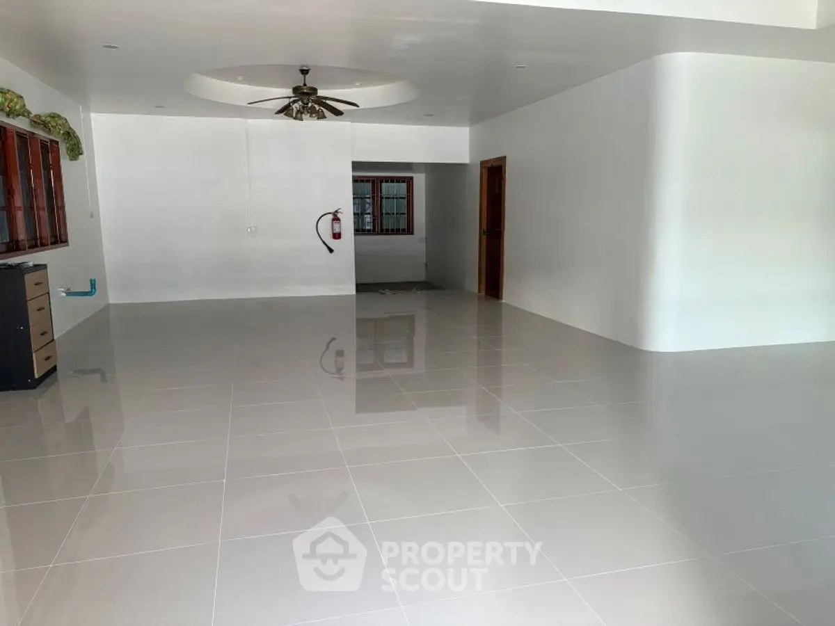 Spacious empty room with glossy tiled floor and ceiling fan, ideal for customization.