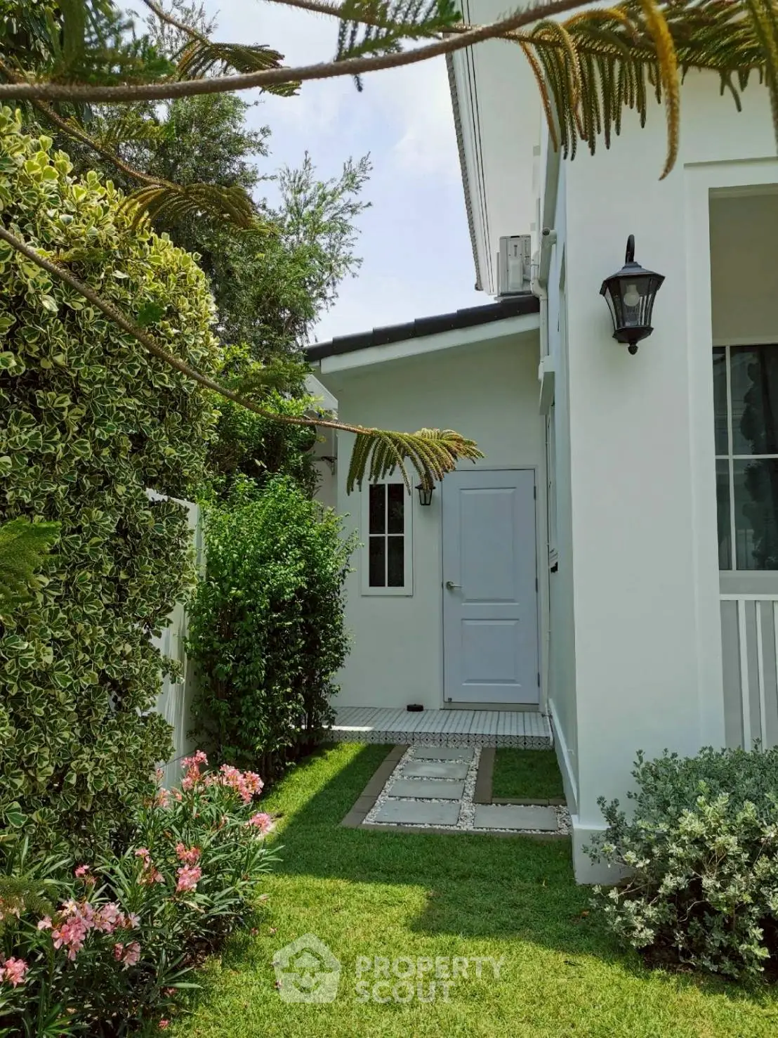 Charming white house exterior with lush garden and pathway, perfect for serene living.