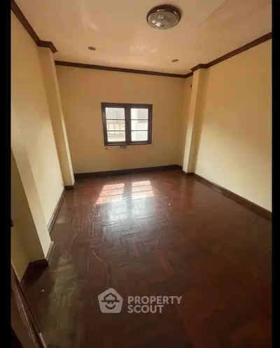 Spacious empty room with wooden flooring and natural light from window.