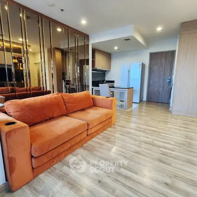 Modern open-layout living room with orange sofa and sleek kitchen area, perfect for stylish urban living.