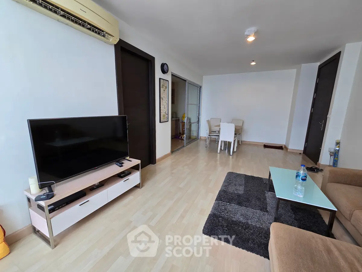 Spacious living room with modern decor and dining area, featuring a sleek TV setup and cozy seating.