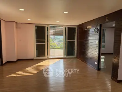 Spacious living room with large windows and wooden flooring, offering ample natural light and a serene view.