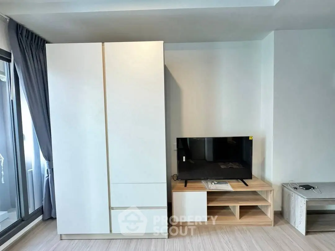 Modern living room with sleek wardrobe and flat-screen TV, featuring large windows and stylish decor.
