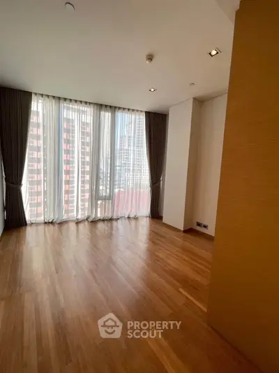 Spacious empty room with large windows and wooden flooring in modern apartment.