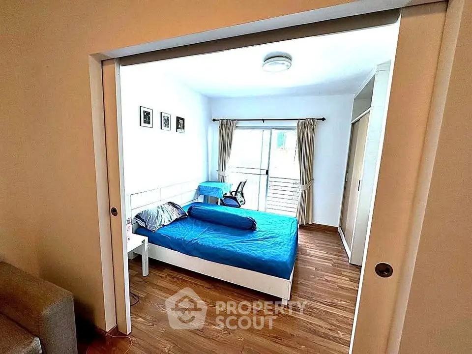 Spacious bedroom with wooden flooring and sliding doors, featuring a cozy bed and natural light.