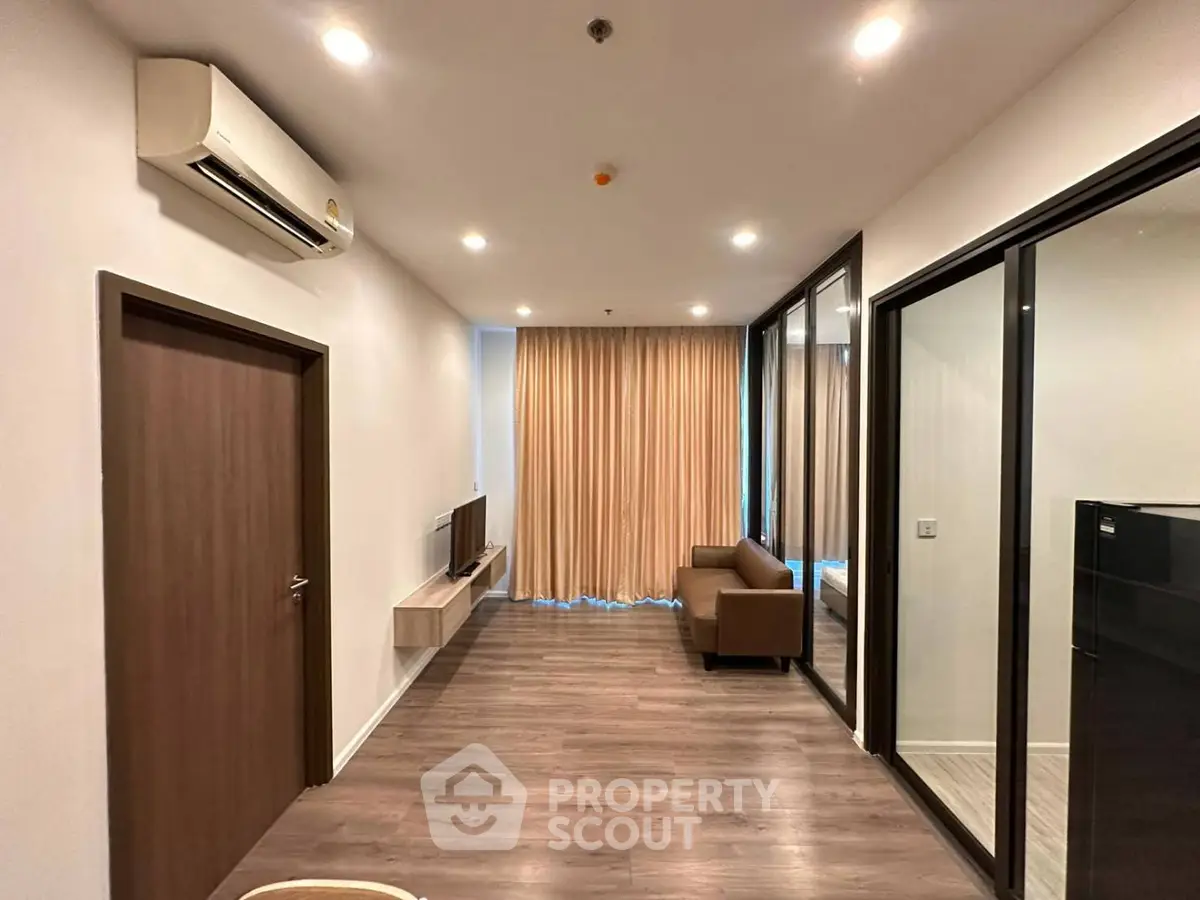 Modern living room with wooden flooring, air conditioning, and large windows with curtains.