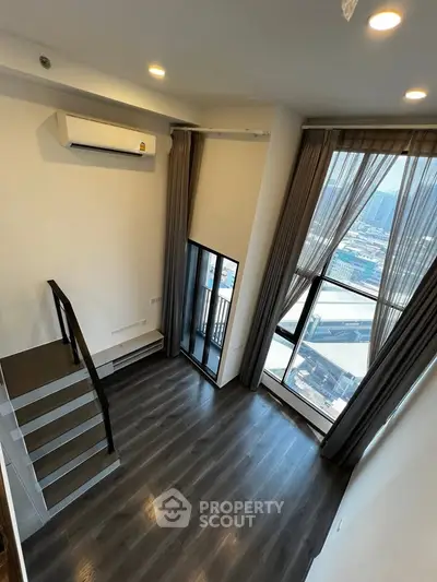 Modern loft-style living room with high ceilings and large windows offering city views.