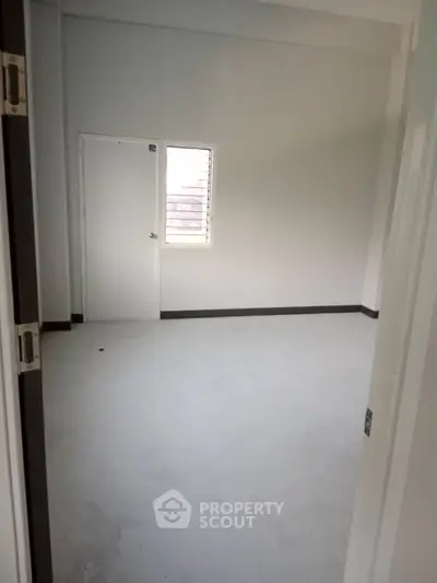 Spacious empty room with white walls and a small window, ideal for customization.