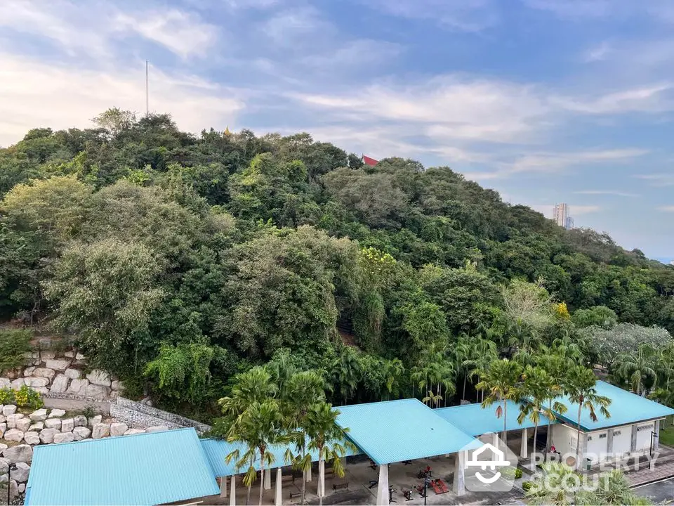 Scenic view of lush green hill with blue-roofed buildings in foreground, perfect for serene living.