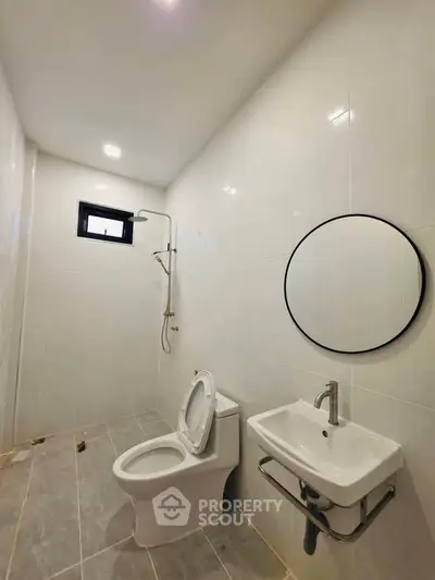 Modern bathroom with sleek fixtures and minimalist design, featuring a round mirror and walk-in shower.
