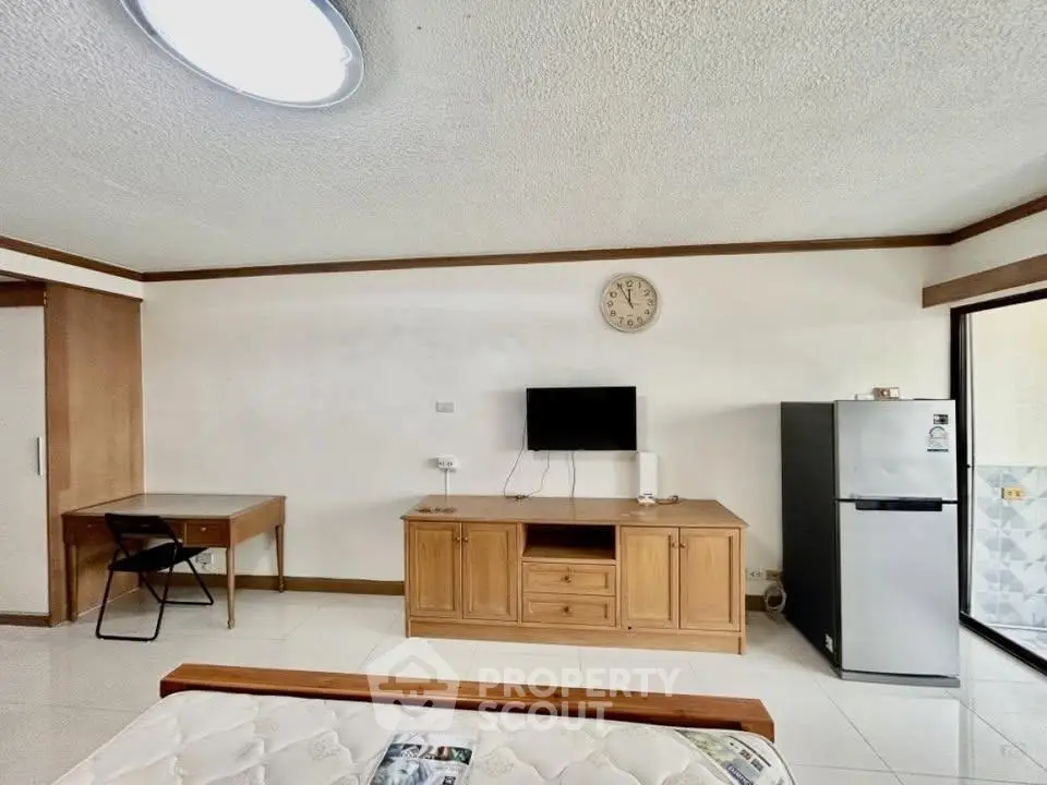 Spacious living area with modern furniture and appliances, featuring a wall-mounted TV and a sleek refrigerator.