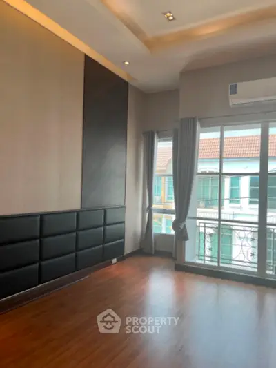 Elegant living space with polished wooden floors, sophisticated cove lighting, and a quaint balcony offering a serene suburban view.