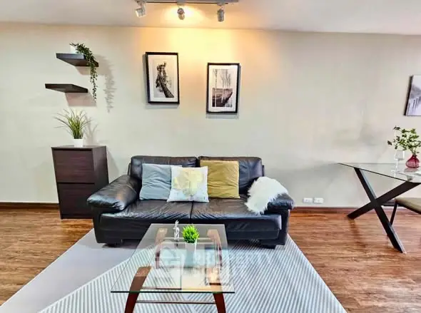 Stylish living room with modern decor, featuring a sleek black sofa, glass coffee table, and elegant wall art.