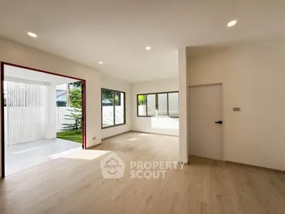 Spacious and bright living room with large windows and modern flooring, opening to a serene outdoor area.