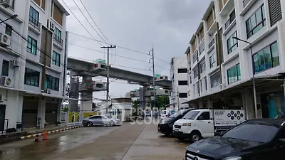 Modern urban building complex with parking area and elevated train tracks in the background.