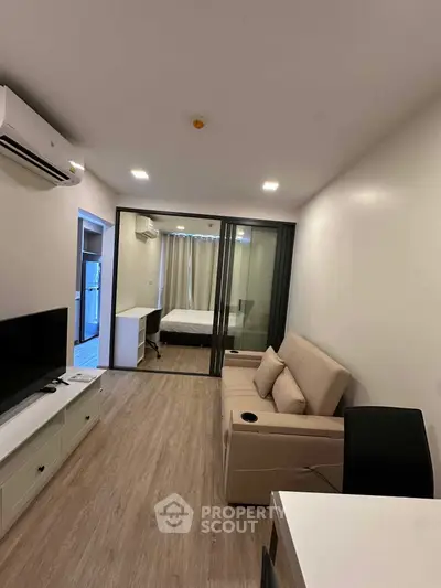 Modern apartment interior with open living room and bedroom, featuring sleek design and natural lighting.