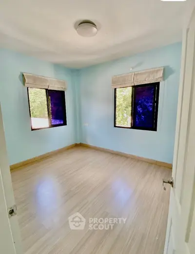 Bright empty bedroom with wooden flooring and two large windows.