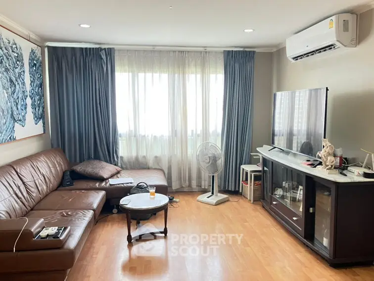 Spacious living room with leather sofa, large window, and modern entertainment setup.