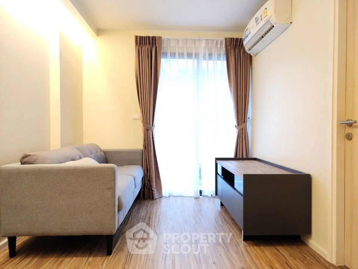Cozy living room with modern sofa and wooden flooring, featuring natural light from large window.