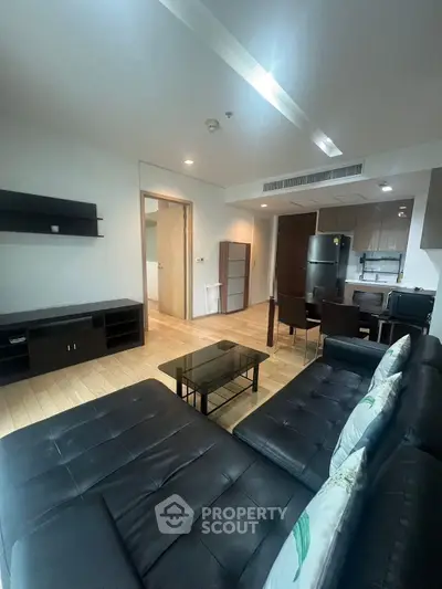 Modern living room with sleek black leather sofa and open kitchen layout in stylish apartment.