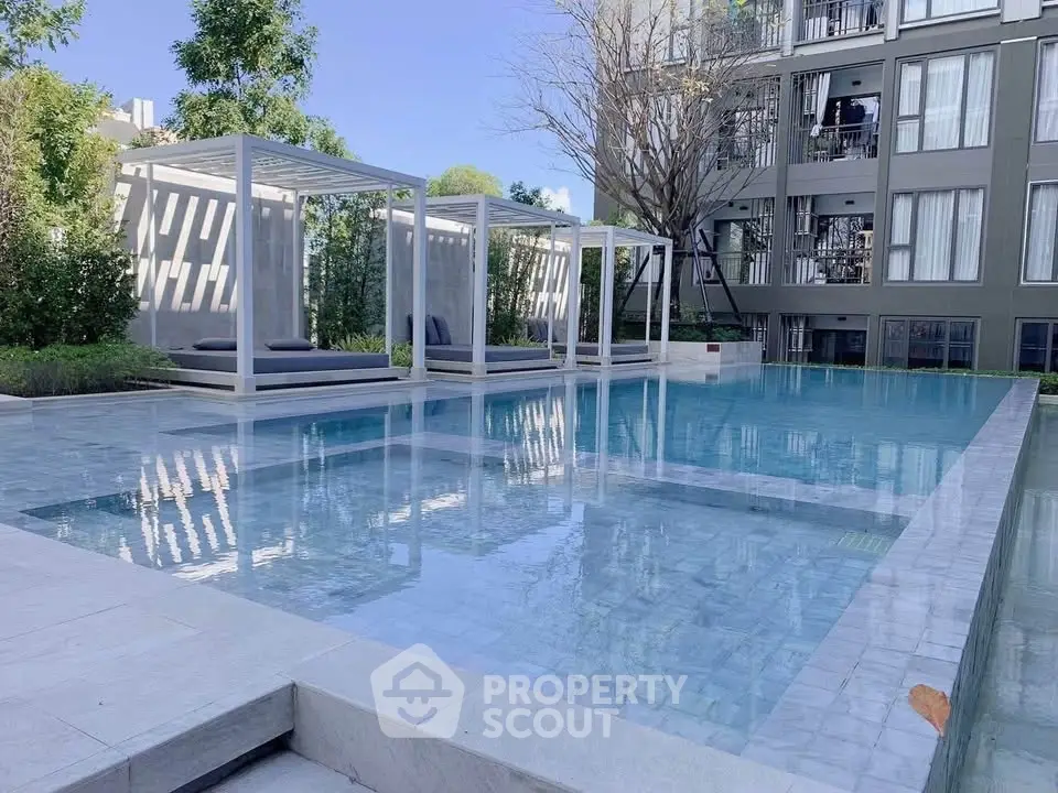 Luxurious modern apartment complex with serene poolside cabanas and lush greenery.