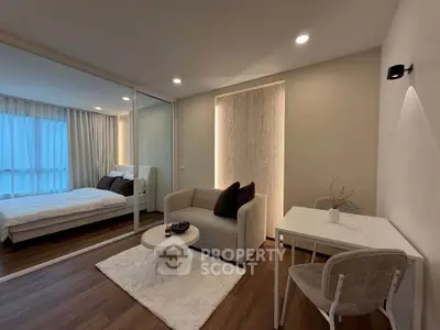 Modern living room with cozy seating and view into elegant bedroom through glass partition.
