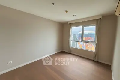 Spacious empty room with large window and wooden flooring in modern apartment.