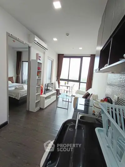 Modern open-plan apartment with sleek kitchen and bright living area, featuring large windows and stylish decor.
