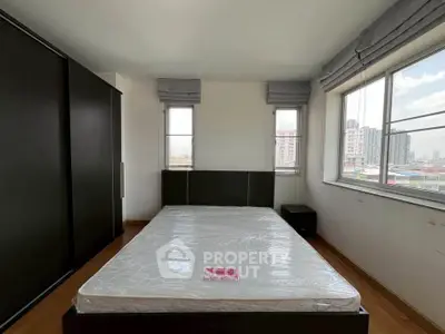 Spacious bedroom with large windows and city view, featuring a modern bed and ample storage.