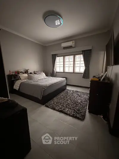 Spacious bedroom with cozy decor and natural light, featuring a comfortable bed and modern air conditioning.