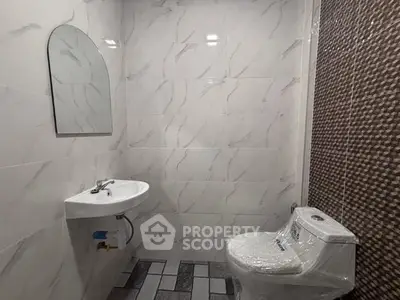 Modern bathroom with sleek design and tiled walls, featuring a compact sink and toilet.