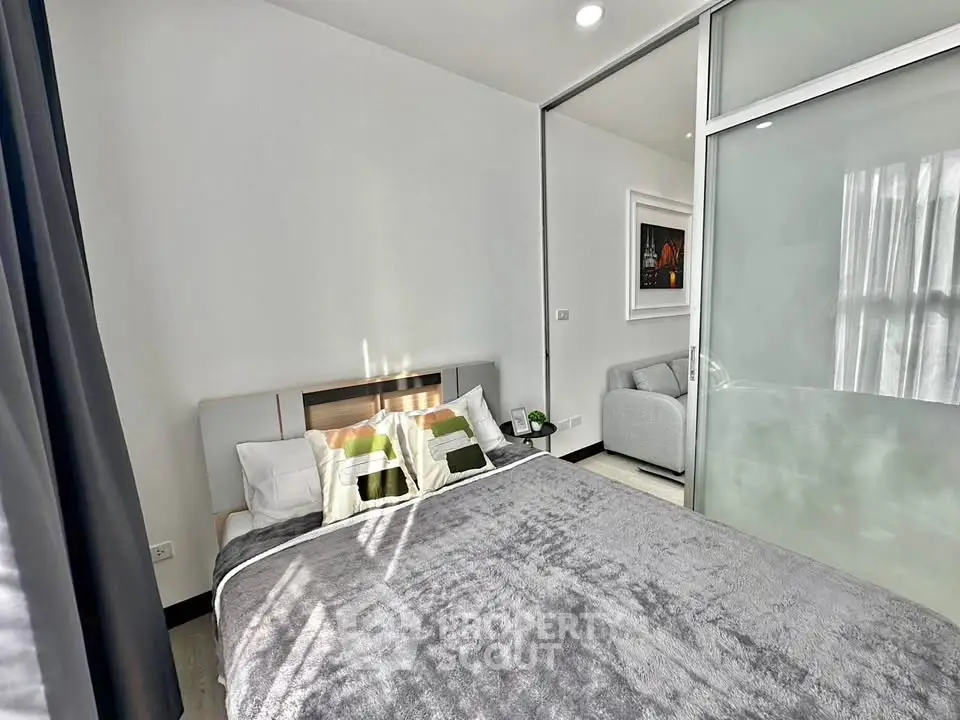 Modern bedroom with cozy bed and sliding glass door leading to a stylish living area.