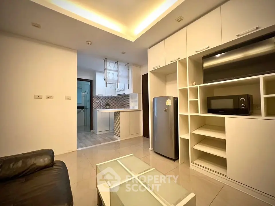 Modern living room with sleek kitchen and built-in storage, featuring contemporary lighting and tiled flooring.