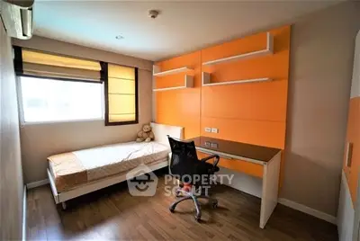 Modern bedroom with built-in desk and shelving, featuring bright orange accents and a cozy single bed.