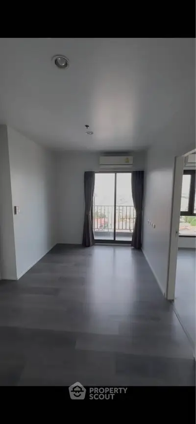 Spacious modern living room with large window and balcony access, featuring sleek flooring and neutral tones.