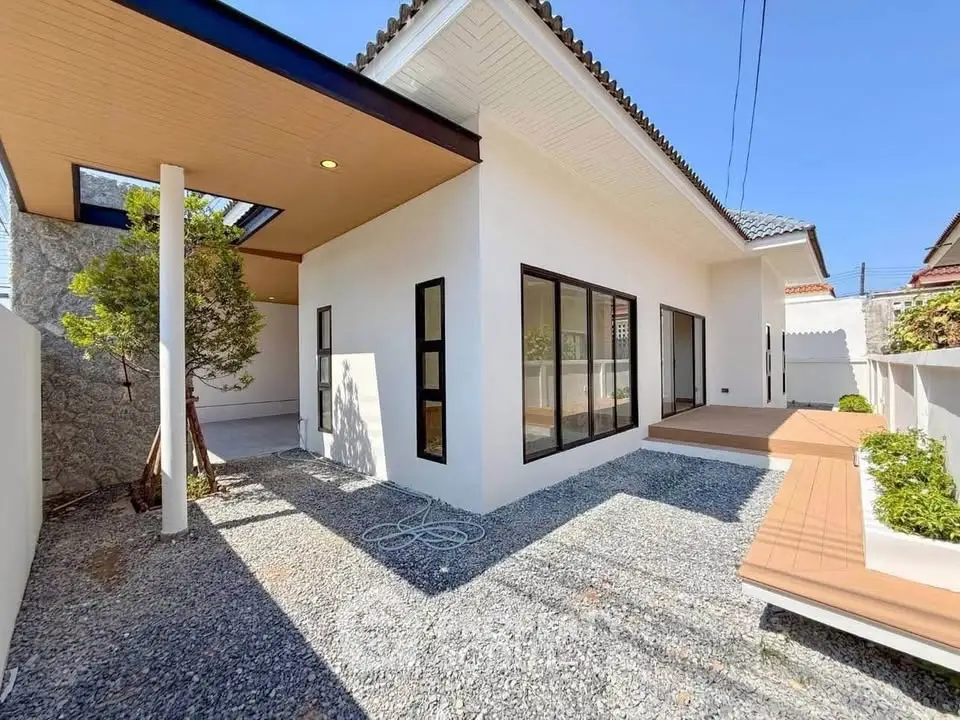 Modern minimalist house exterior with clean lines and large windows, featuring a gravel pathway and wooden deck.
